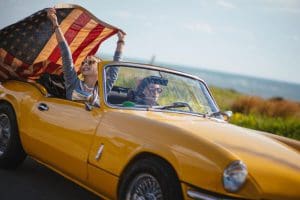 Young women with American flag driving a yellow convertible