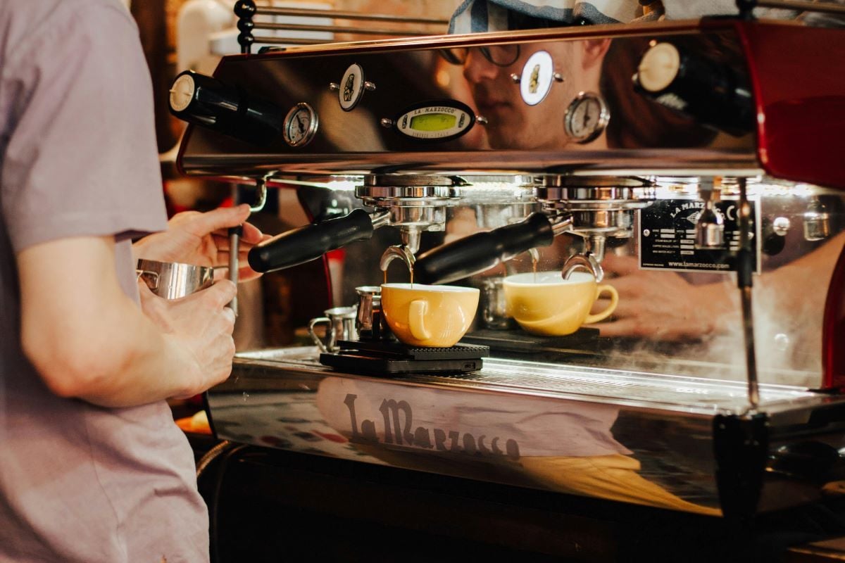 A pair of hands using a cappuccino machine in a café.