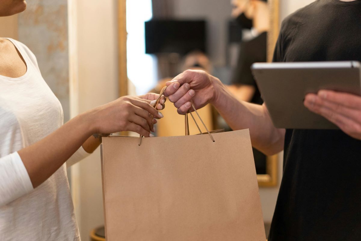 Person holding a tablet handing a bag a to a customer